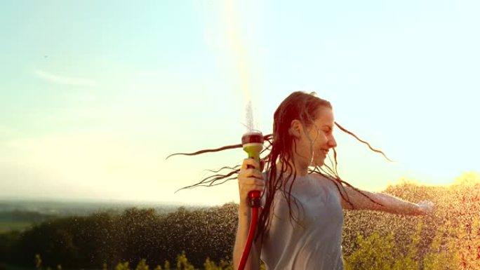 超级SLO MO年轻女子开心地用花园水管喷水