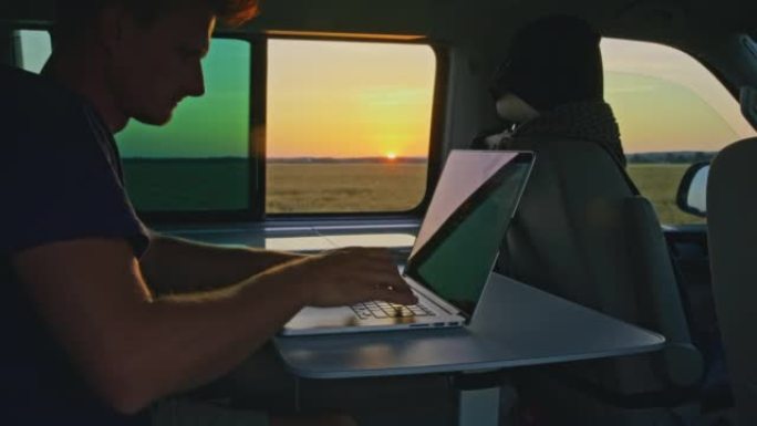 WS男子在日落时停在乡下的露营车内的笔记本电脑上工作