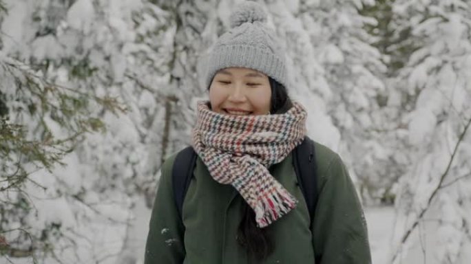 冬天站在森林里看着相机微笑的快乐女游客的慢动作肖像