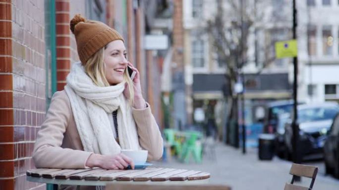 秋季，女性顾客坐在繁忙的城市大街上的咖啡店外打电话给手机