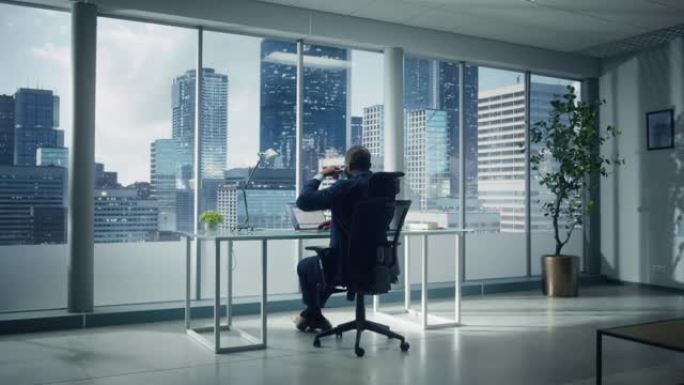 成功的非洲裔美国商人坐在他的办公桌前，在他的大城市办公室里用笔记本电脑工作。帅公司CEO规划电子商务