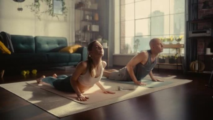 运动年轻夫妇一起锻炼，伸展运动，早上在家里阳光明媚的房间里做瑜伽。穿着运动服的美丽男人和女人在垫子上