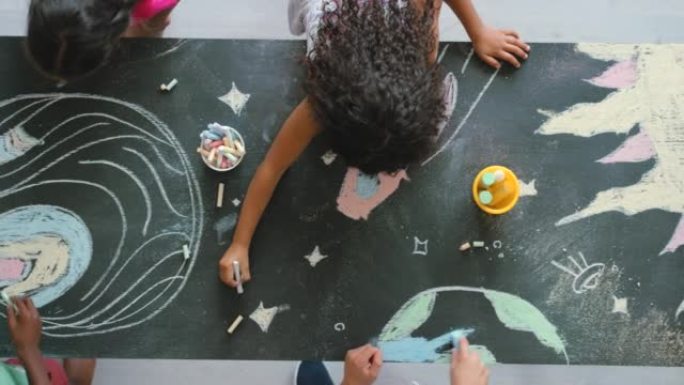 富有创造力的幼儿在黑板上用粉笔绘画和制作彩色的空间图片。上面是孩子们给行星和恒星着色的视图。艺术学生