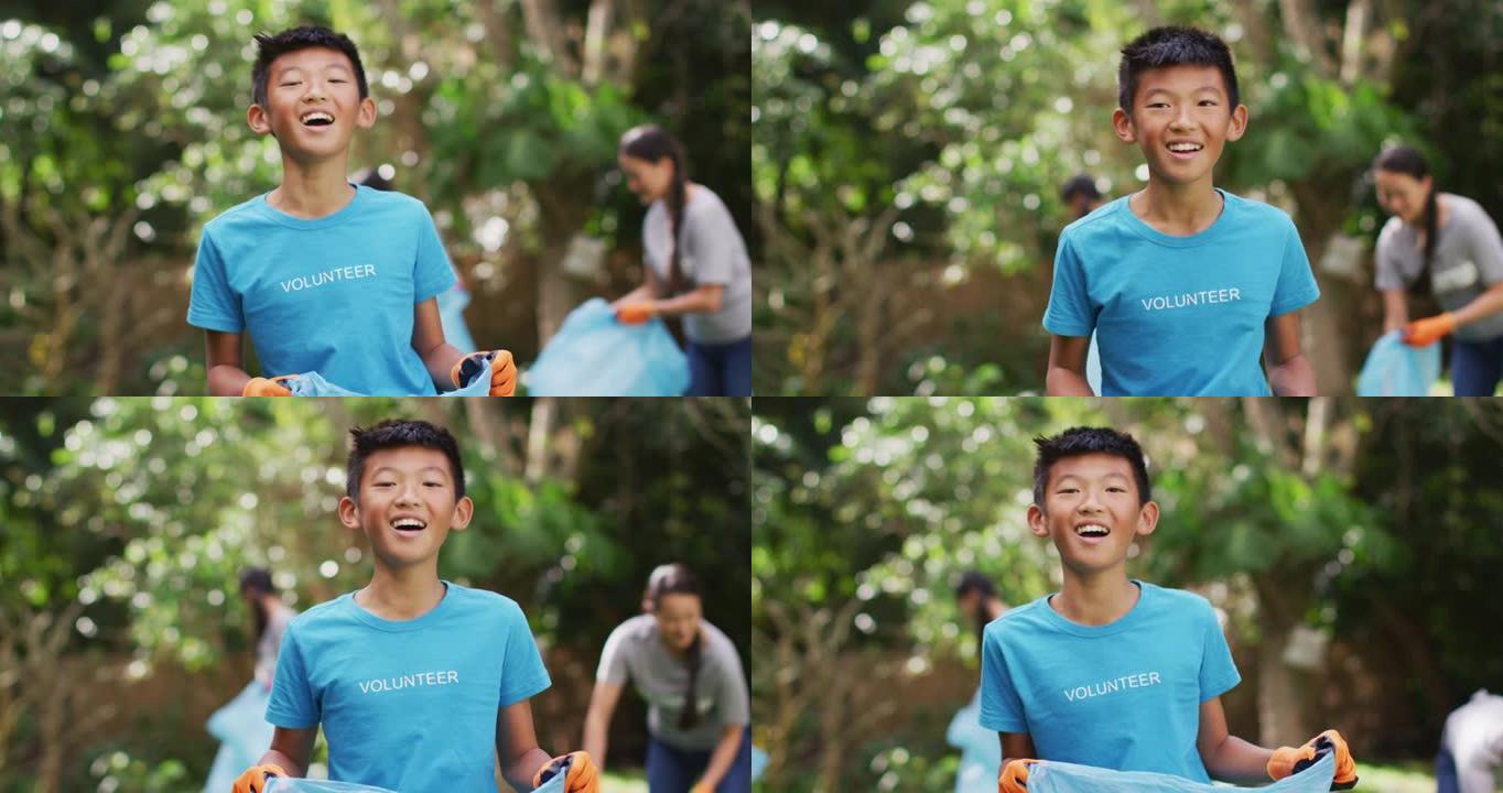 穿着志愿者t恤拿着垃圾袋收集塑料垃圾的亚洲男孩笑