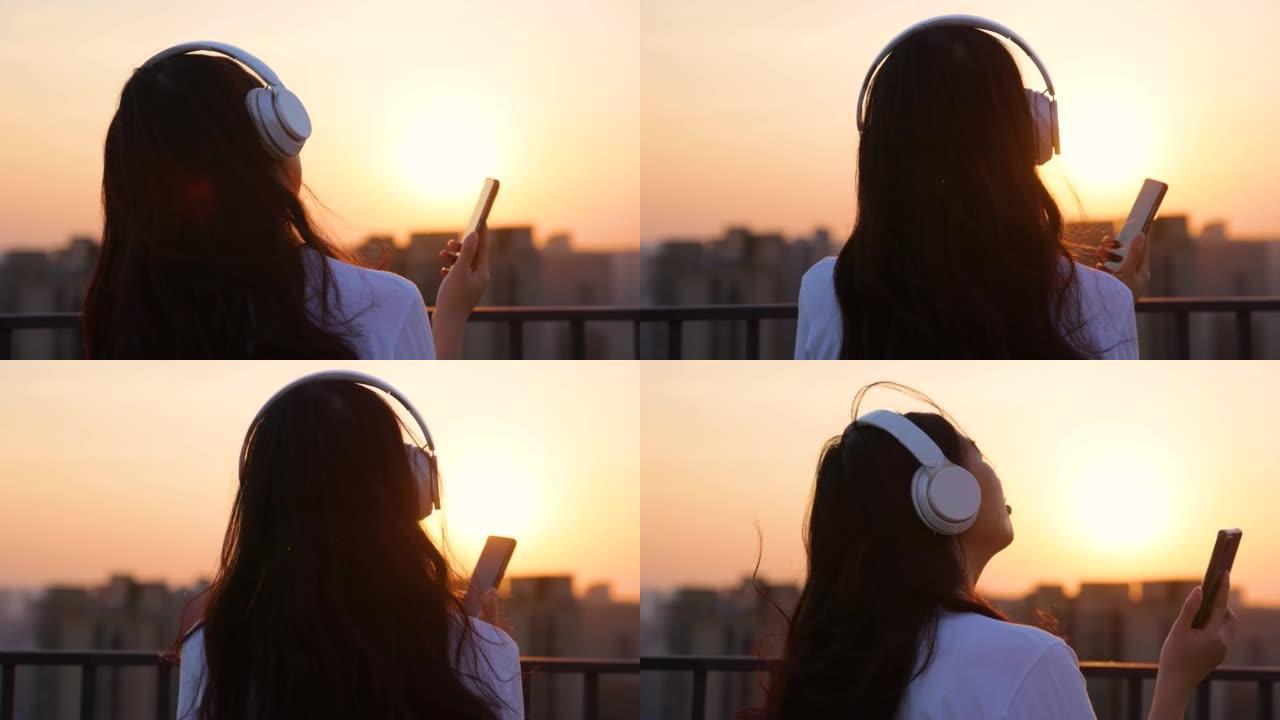 日落时听音乐耳机的女孩在日落时听音乐