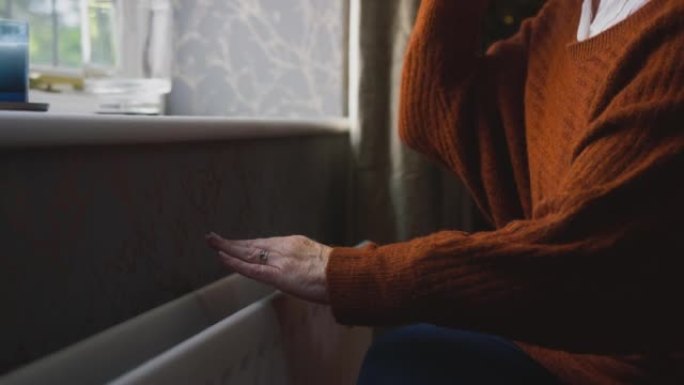 在能源危机中，老人喝热饮料试图在家中通过散热器保暖的特写镜头