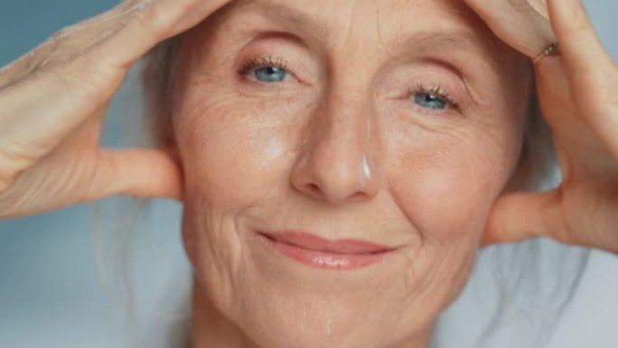 美丽的高级女人轻轻涂抹面霜的肖像。老年女士用天然抗衰老化妆品使皮肤柔软、光滑、无皱纹。美容护肤产品。