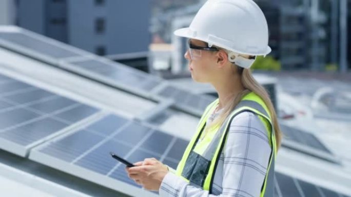 一位认真的年轻女子在建筑物的屋顶上安装太阳能电池板时使用智能手机。一位专注的女性在网上使用手机进行可