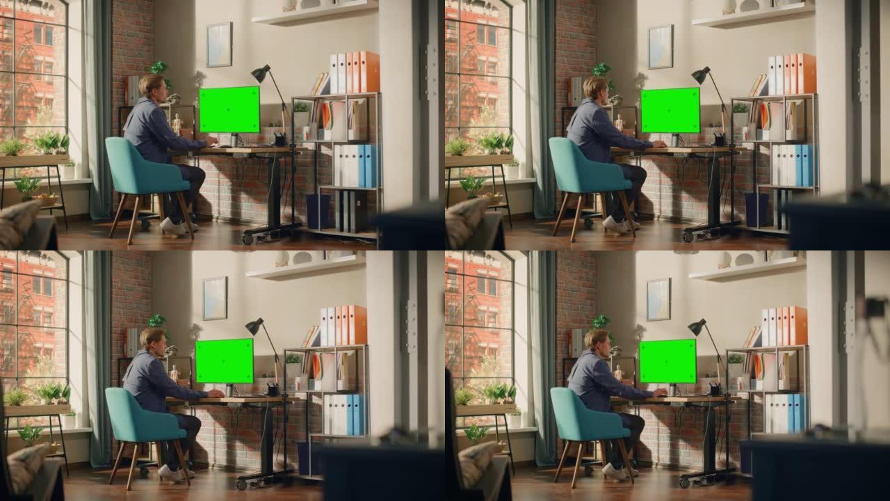年轻英俊的男人在家工作，在带有绿屏模拟显示的台式计算机上。创意男性查看社交媒体，浏览互联网。明亮阁楼