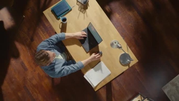 俯视图缩小镜头: 坐在办公桌前的自由企业家打开笔记本电脑并开始工作。远程访问专业人员撰写电子邮件，管