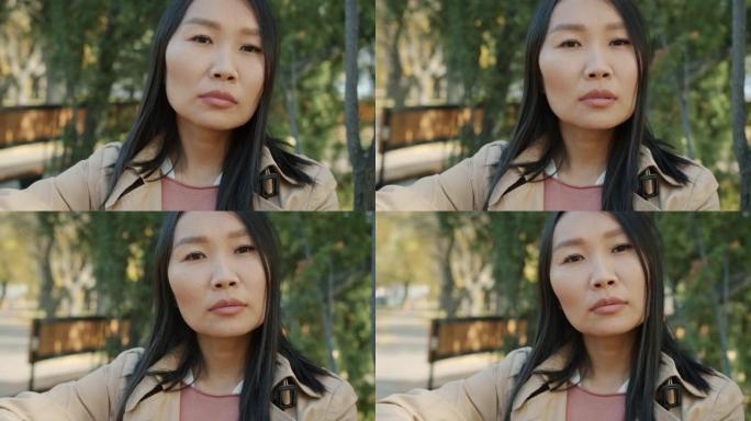 秋天公园外面看着相机的沉思亚洲女士的特写慢动作肖像