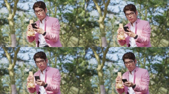 亚洲男子坐在公园里吃零食并使用智能手机