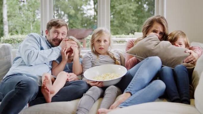 受惊的家人坐在家里的沙发上，用爆米花在电视上看恐怖电影