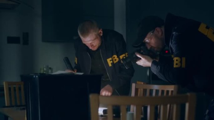 在一间暗室里，两名身穿制服的白人联邦调查局探员拿着手电筒和照相机，在桌子上检查物证。FBI特工的动作