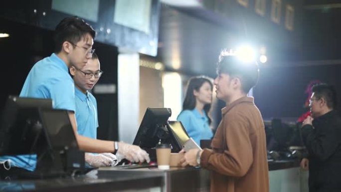 亚洲华裔年轻人在电影院电影放映时间前购买爆米花和饮料，非接触式付款