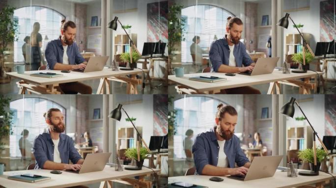时尚的长发胡须专家坐在创意机构的办公桌前。年轻的时尚男人在营销公司的笔记本电脑上工作。后台的办公室团