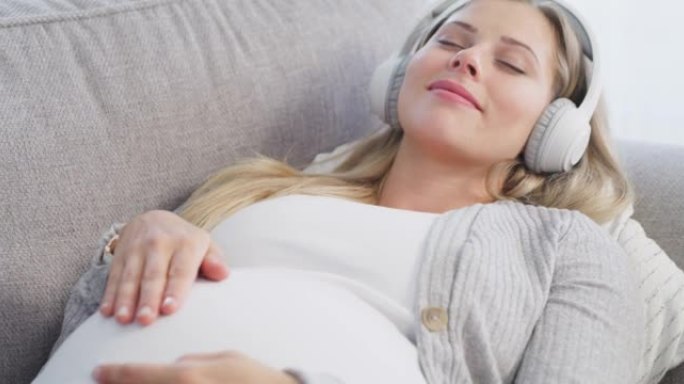 4k视频片段，一名怀孕的年轻女子在沙发上放松时听音乐
