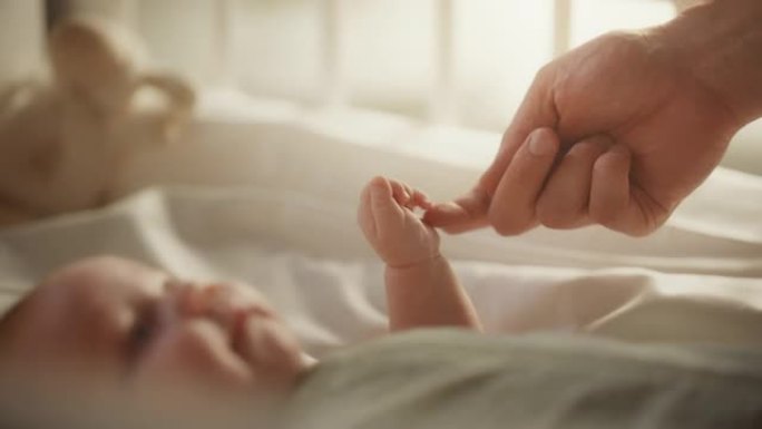 特写婴儿躺在婴儿床的背部时，用母亲的手和手指玩耍的镜头。高加索新生儿蹒跚学步的孩子和妈妈在一起。童年