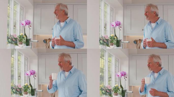 退休的老人站在家里的厨房里看着窗外喝咖啡-慢动作射击