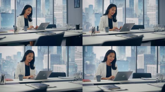 在大城市办公室，穿着时髦西装在笔记本电脑上工作的成功亚洲女商人的肖像。强大的CEO管理数字电子商务项