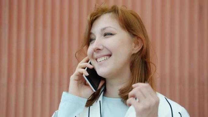 年轻的红发女士在手机上聊天，在户外大笑的肖像
