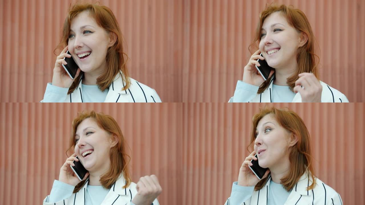 年轻的红发女士在手机上聊天，在户外大笑的肖像
