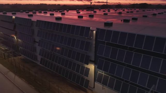 航空移动平行镜头，多个现代太阳能电池板连接到物流大楼的工业仓库。黄昏黄昏日落，云彩轻盈，粉色。