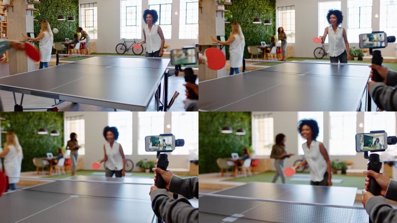 乒乓球、电话和视频，一名女员工和她的同事在办公室休息室玩得开心。创意设计办公室初创公司中的团队建设，