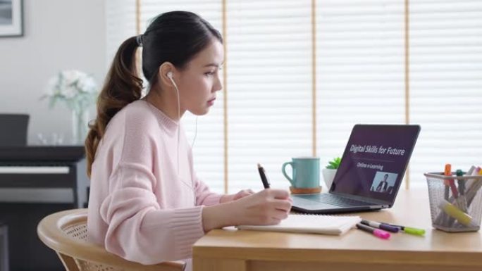 侧视图年轻的亚洲女性听观看数字课程在线学习员工技能在家庭办公室的笔记本电脑上提高技能。针对成人的商学