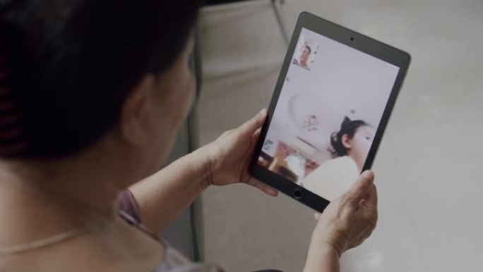 4k分辨率手持射击亚洲高级妇女手持平板电脑设备，并通过视频通话或视频会议技术与孙女交谈，同时在冠状病