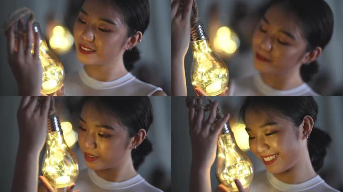 一个美丽的亚洲中国少女看着并拿着一个带发光二极管灯串的灯泡微笑