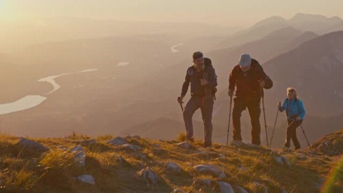SLO MO三个徒步旅行者在日落时走在山脊上