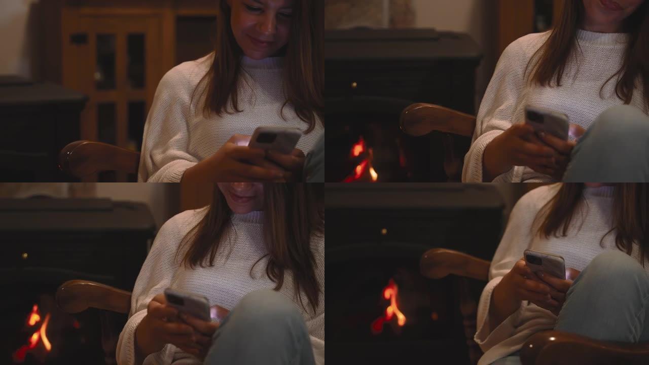 女人在家在壁炉旁的椅子上放松时使用手机