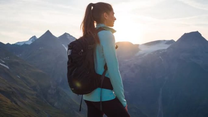 女人站在山顶上，在日落时欣赏周围山脉的壮丽景色