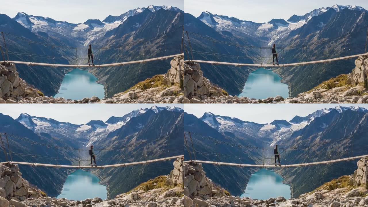 年轻的女徒步旅行者从山溪上的悬吊桥上欣赏壮丽的山谷湖景色
