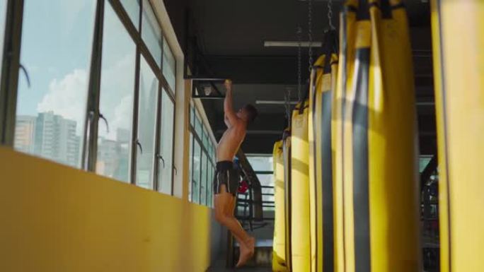 亚洲马来运动员在健身房健身俱乐部锻炼身体，在窗口白天时间旁边有一排黄色出气筒沙袋
