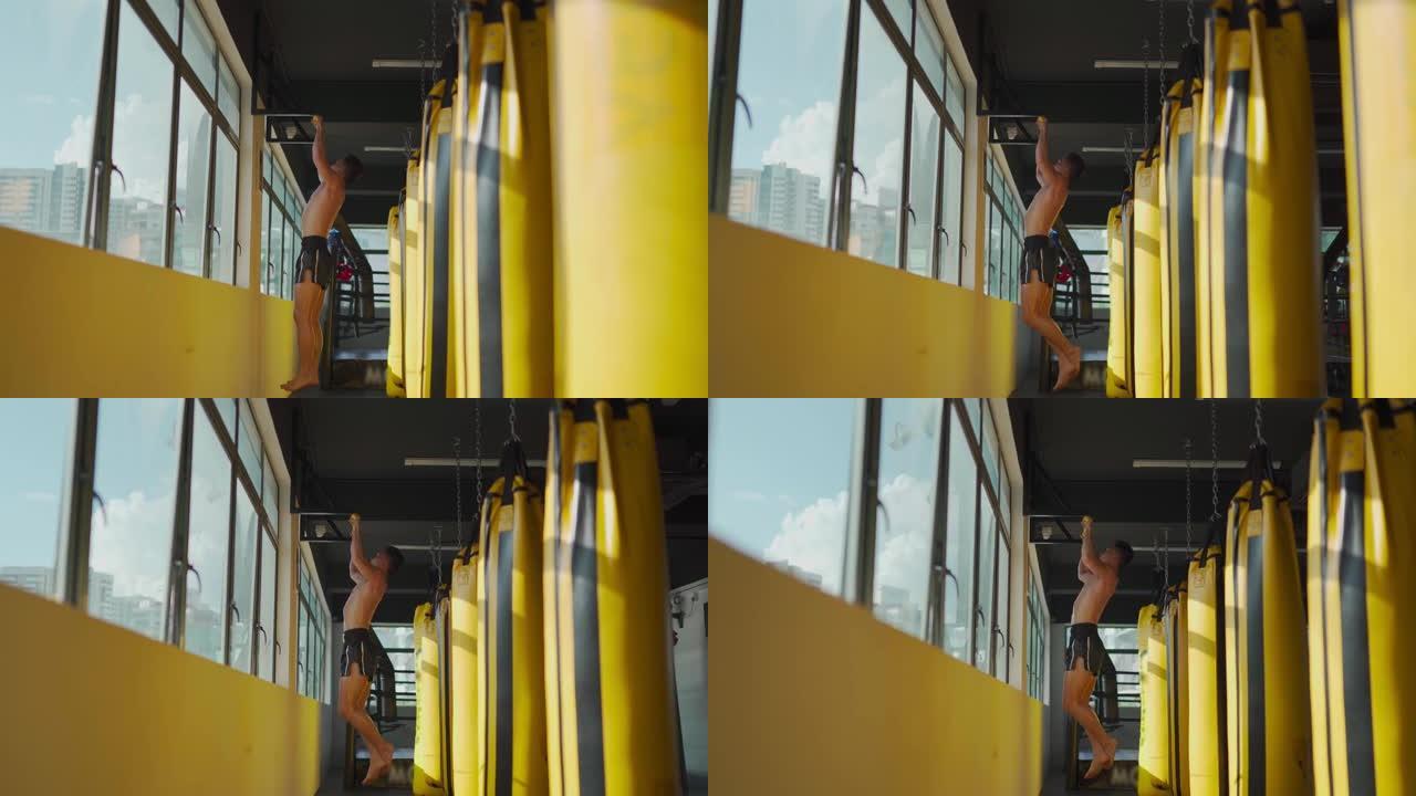 亚洲马来运动员在健身房健身俱乐部锻炼身体，在窗口白天时间旁边有一排黄色出气筒沙袋