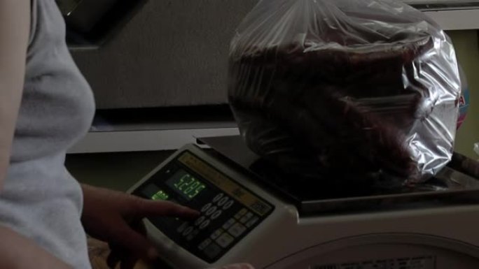 女杂货店工作人员使用电子秤检查蔬菜成本。特写。