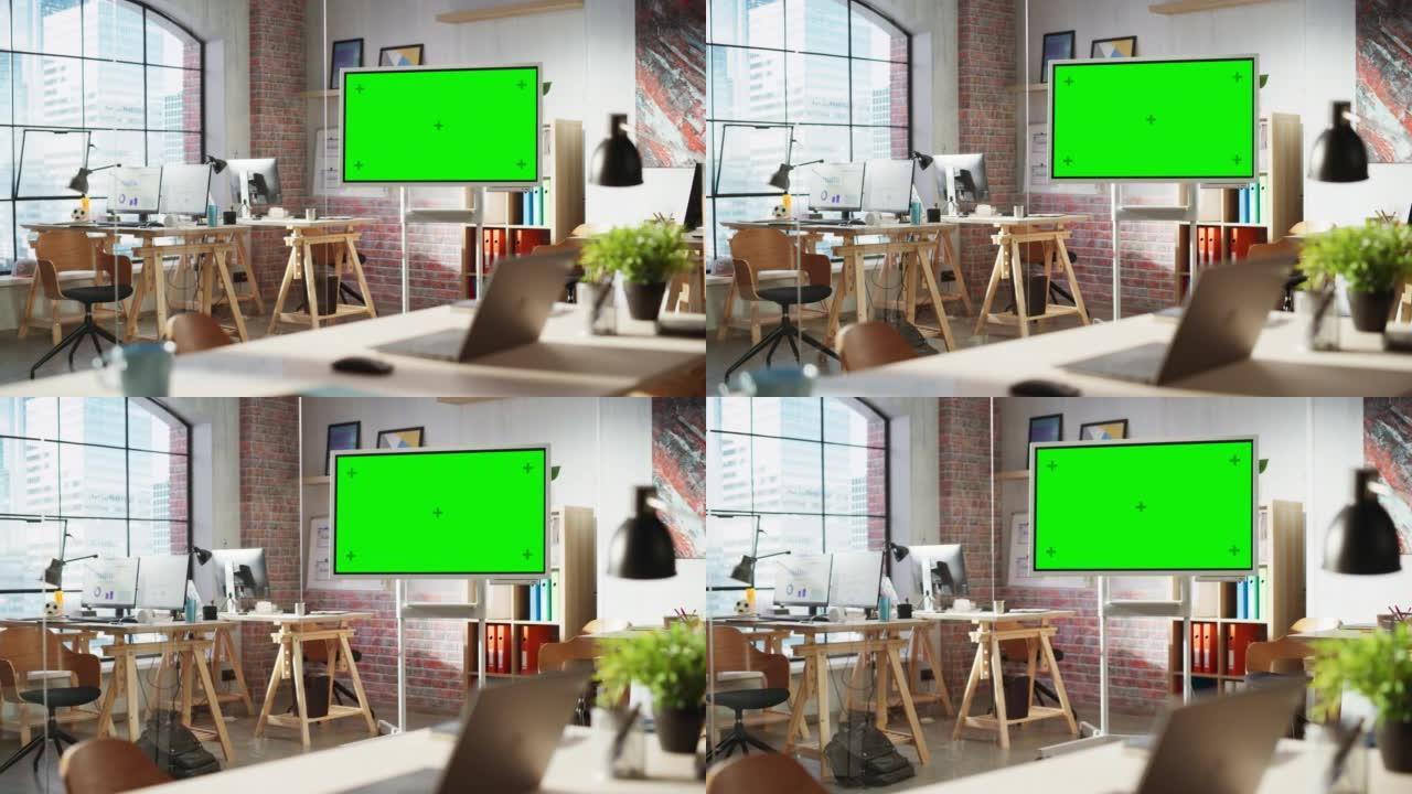 现代创意机构的团队会议空会议室，墙壁上有艺术品，桌子上有电脑。带有数字绿屏模拟色度键显示器的办公空间