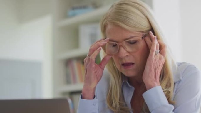 更年期成熟妇女戴着眼镜在笔记本电脑上工作，患有慢动作头痛