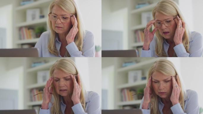 更年期成熟妇女戴着眼镜在笔记本电脑上工作，患有慢动作头痛