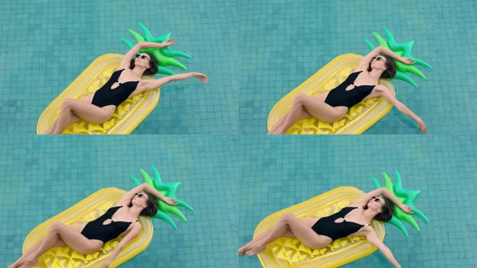 充气菠萝上的快乐女人漂浮在游泳池里享受夏天，穿着性感比基尼度假放松