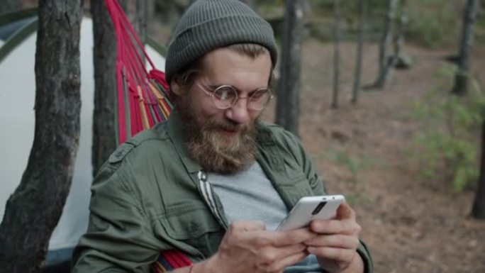 年轻人游客使用智能手机触摸屏，在森林的吊床上放松