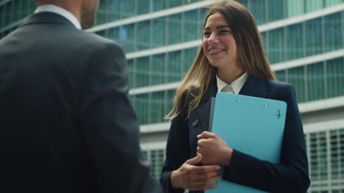 在正式服装中微笑的商业伙伴的电影镜头在开始在摩天大楼背景上开会之前握手。企业、财务、交易、成功、合作