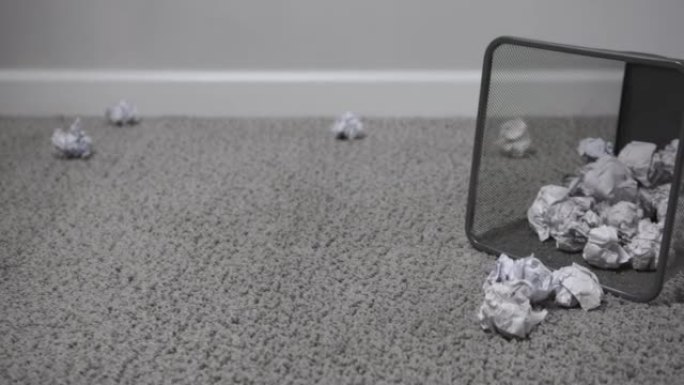 白色皱巴巴的纸球飞入黑色方形废纸篓，躺在明亮的房间的灰色地毯上