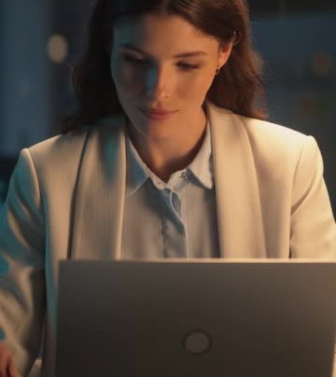 垂直屏幕: 晚上在公司办公室工作的女性在笔记本电脑上工作。年轻的经理浏览互联网，在线购物并阅读朋友和