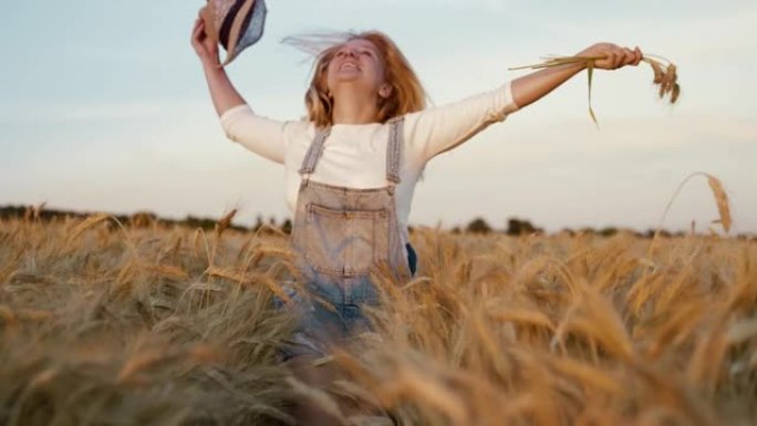 无忧无虑的女人在田间奔跑时拿着小麦和草帽