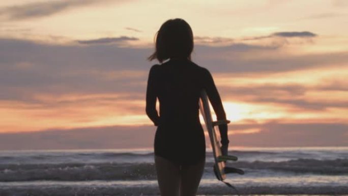 日落时在热带海滩上与冲浪板一起跑步的冲浪女孩的剪影。