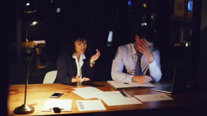 两个疲惫的商人晚上在办公室一起工作时谈论报告和文件。男女专业同事集思广益，试图在截止日期前完成