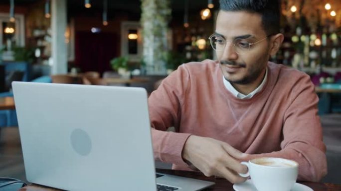 在尼斯咖啡馆用笔记本电脑喝咖啡的阿拉伯年轻人的慢动作肖像